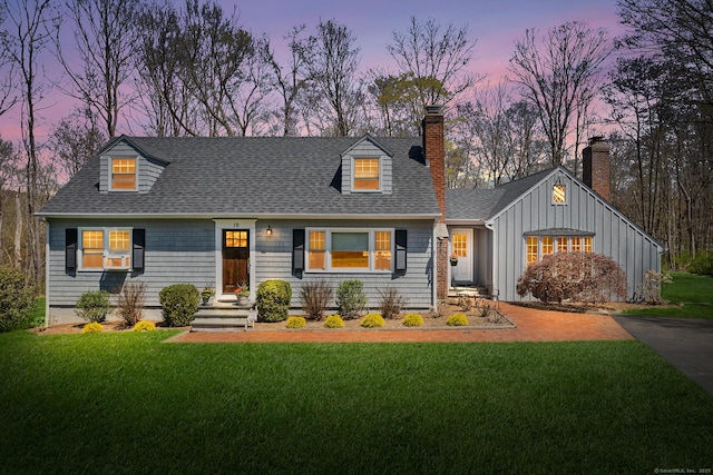 cape cod house with a lawn, board and batten siding, a chimney, and roof with shingles