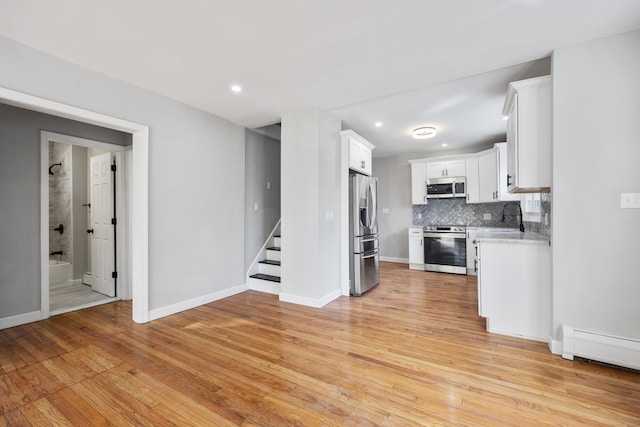 kitchen featuring tasteful backsplash, stainless steel appliances, light wood finished floors, and white cabinets