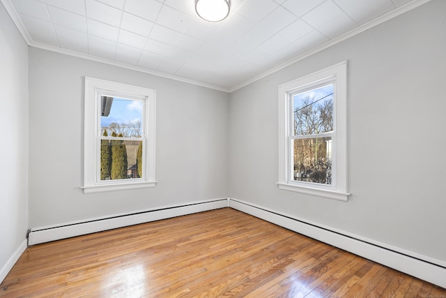spare room featuring crown molding, a baseboard heating unit, a wealth of natural light, and wood-type flooring