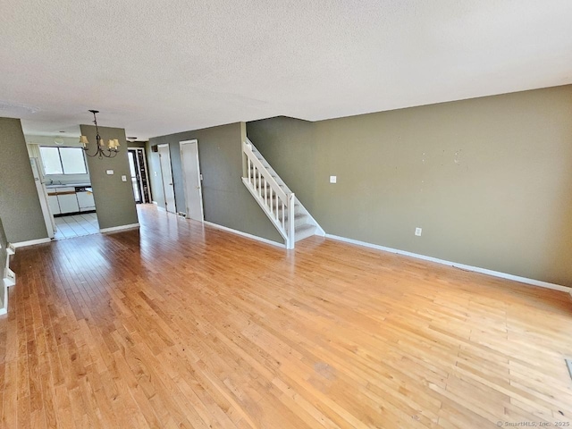 unfurnished living room featuring a textured ceiling, stairway, a chandelier, baseboards, and wood finished floors