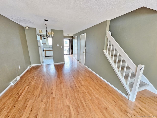 unfurnished dining area featuring a textured ceiling, light wood-style flooring, visible vents, a notable chandelier, and stairs