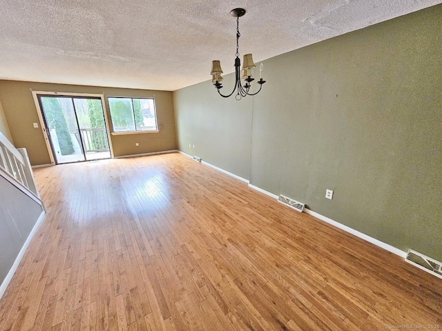 unfurnished dining area featuring light wood-style flooring, a chandelier, baseboards, visible vents, and a textured ceiling