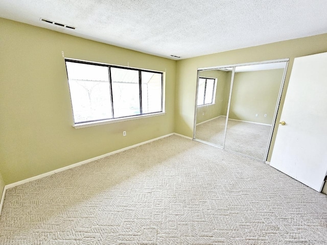 unfurnished bedroom featuring a textured ceiling, carpet flooring, visible vents, baseboards, and a closet