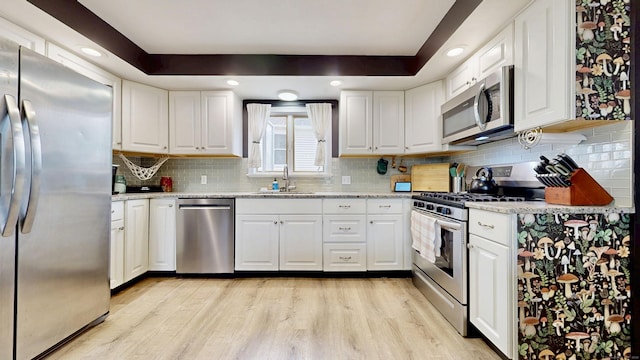 kitchen featuring white cabinetry, tasteful backsplash, light wood-style flooring, a sink, and appliances with stainless steel finishes