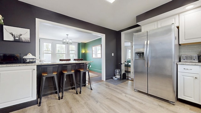kitchen with white cabinets, light wood-style flooring, decorative backsplash, and stainless steel fridge with ice dispenser