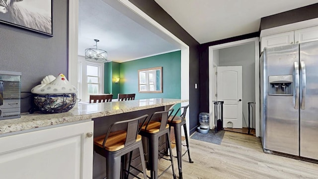 kitchen with light wood-style floors, a breakfast bar area, white cabinetry, light stone counters, and stainless steel fridge with ice dispenser