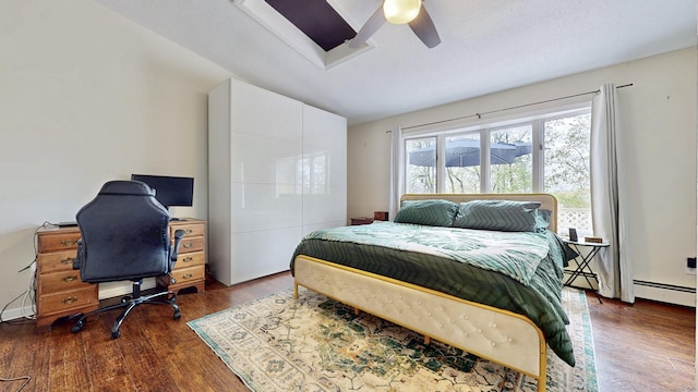 bedroom with a baseboard heating unit, dark wood-style flooring, and ceiling fan