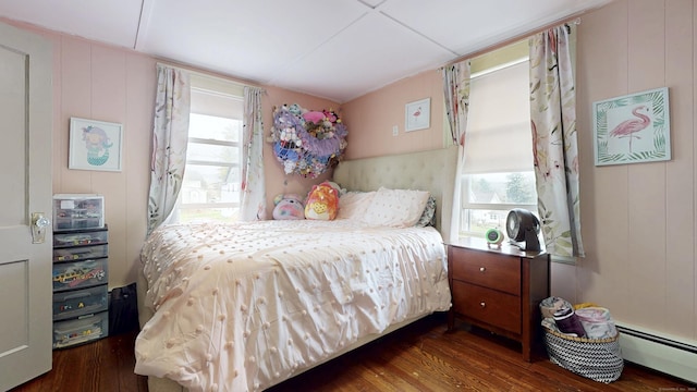 bedroom featuring baseboard heating, wood finished floors, and a decorative wall