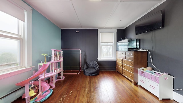 rec room with crown molding, hardwood / wood-style floors, baseboard heating, and a healthy amount of sunlight