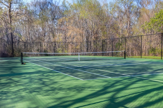 view of tennis court with fence, a view of trees, and community basketball court