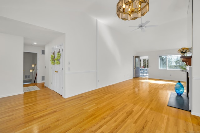 unfurnished living room with light wood-style floors, ceiling fan with notable chandelier, baseboards, visible vents, and high vaulted ceiling