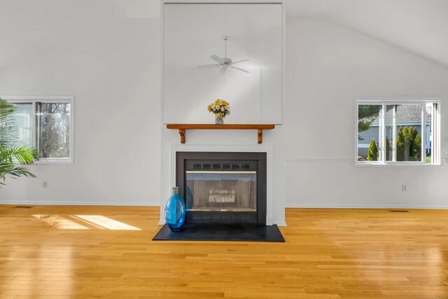 unfurnished living room featuring a fireplace with flush hearth, baseboards, wood finished floors, a ceiling fan, and high vaulted ceiling