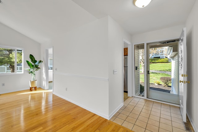 foyer featuring light wood finished floors, a wealth of natural light, lofted ceiling, and baseboards