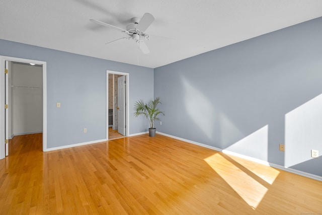 unfurnished bedroom with a closet, a spacious closet, light wood-type flooring, and baseboards