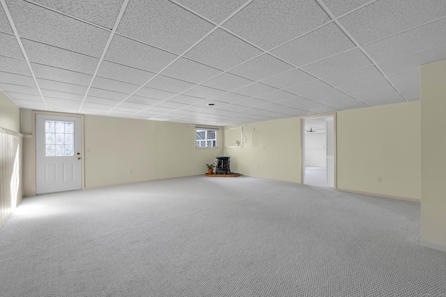 basement featuring carpet, a wealth of natural light, a paneled ceiling, and a wood stove