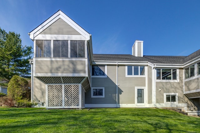 back of property featuring a sunroom, a yard, a shingled roof, and a chimney