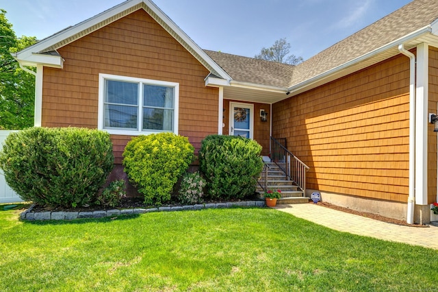 view of exterior entry with a lawn and a shingled roof