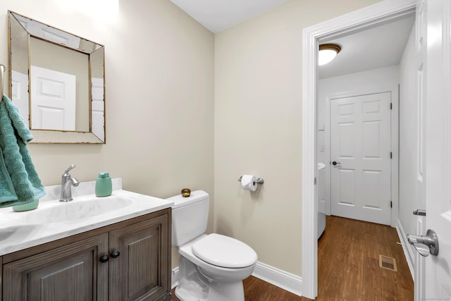 half bath featuring vanity, toilet, baseboards, wood finished floors, and visible vents