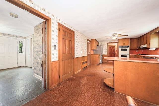30 Sunset Hill Rd, Simsbury, CT 06070 - kitchen with wallpapered walls, stainless steel appliances, ceiling fan, wainscoting, and brown cabinetry