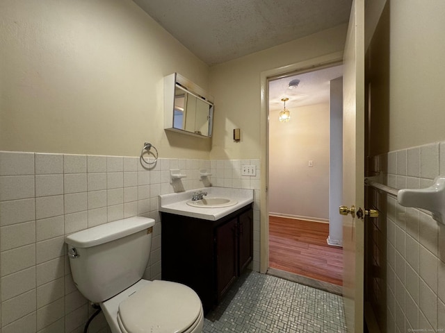 136 Westbury Park Rd Apt C, Watertown, CT 06795 - half bathroom featuring tile walls, tile patterned flooring, toilet, vanity, and a wainscoted wall