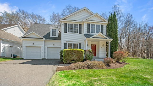 traditional-style home featuring a garage, aphalt driveway, a front yard, and roof with shingles