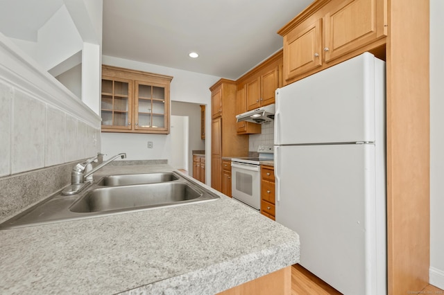 kitchen with a sink, under cabinet range hood, glass insert cabinets, backsplash, and white appliances