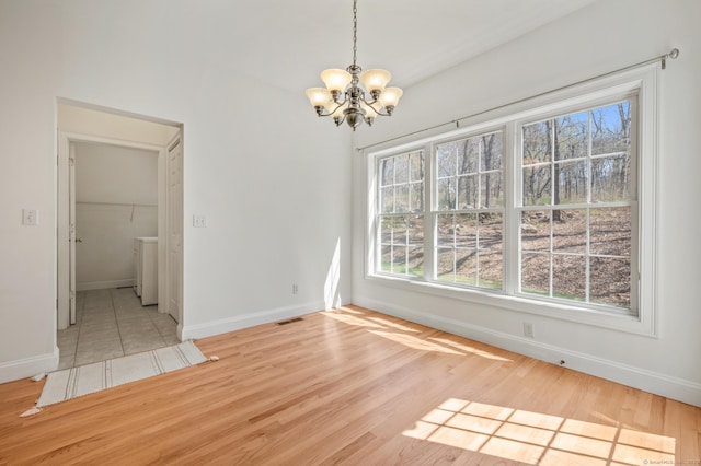 unfurnished dining area with a chandelier, baseboards, a wealth of natural light, and light wood-style flooring