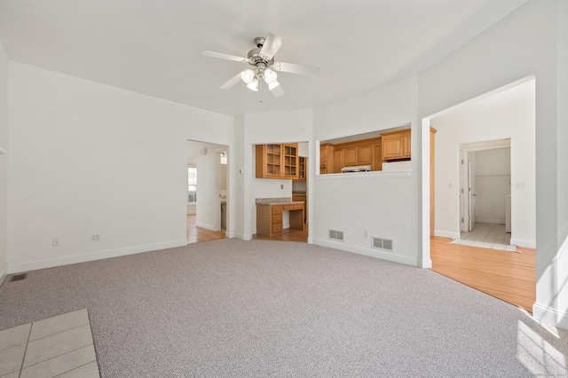 unfurnished living room featuring light colored carpet, visible vents, a ceiling fan, and baseboards