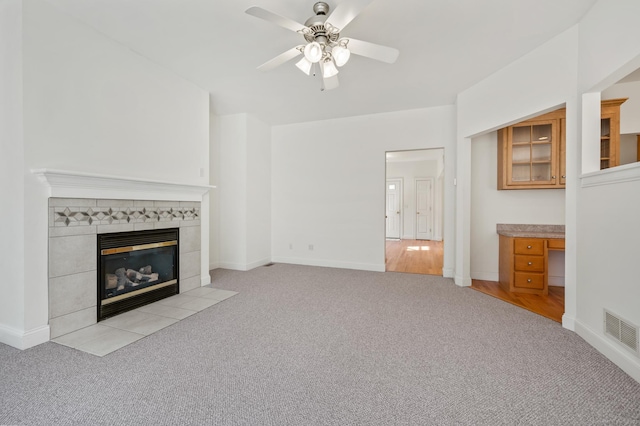 unfurnished living room with a fireplace, a ceiling fan, visible vents, baseboards, and light colored carpet