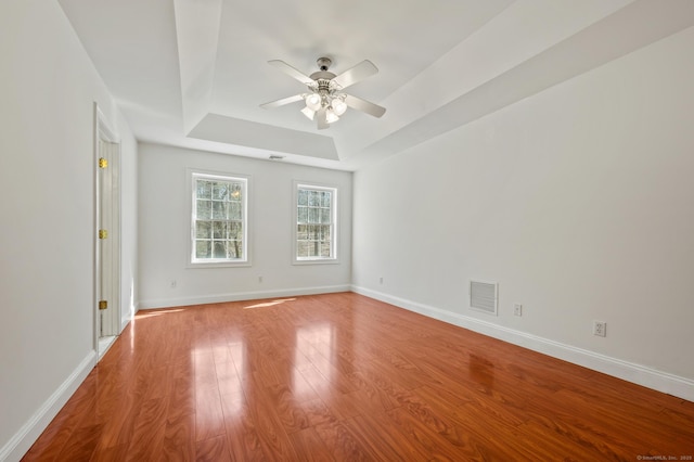 spare room with ceiling fan, a raised ceiling, visible vents, baseboards, and light wood-type flooring