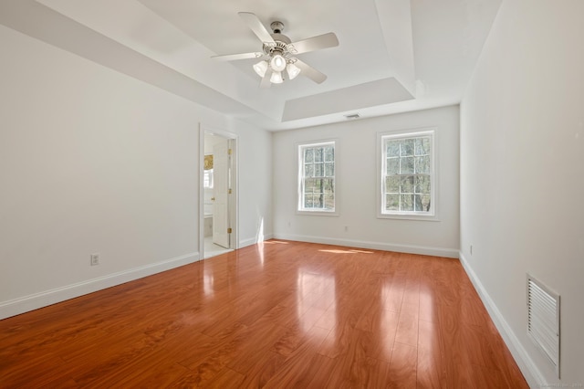 spare room featuring a raised ceiling, visible vents, ceiling fan, light wood-style floors, and baseboards
