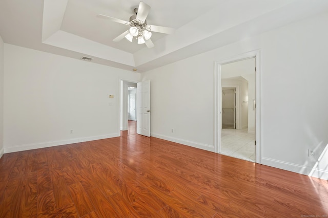 unfurnished room featuring light wood finished floors, baseboards, visible vents, a raised ceiling, and a ceiling fan
