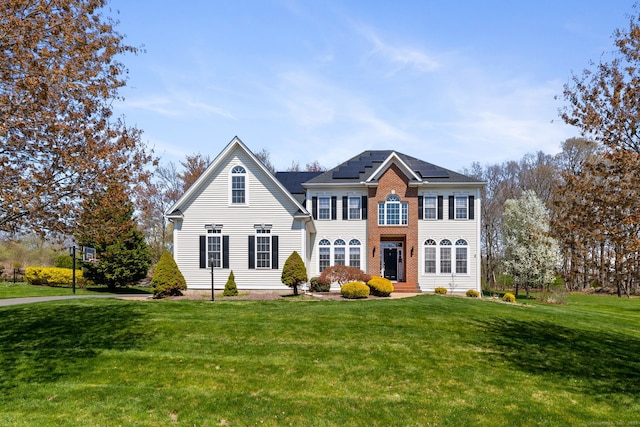 view of front of house featuring roof mounted solar panels, a front lawn, and brick siding