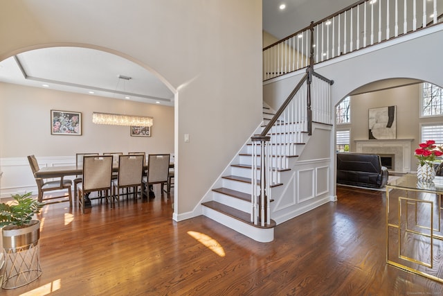 staircase with recessed lighting, a fireplace, a towering ceiling, arched walkways, and wood finished floors