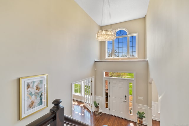 foyer featuring wainscoting, an inviting chandelier, dark wood-type flooring, and a towering ceiling