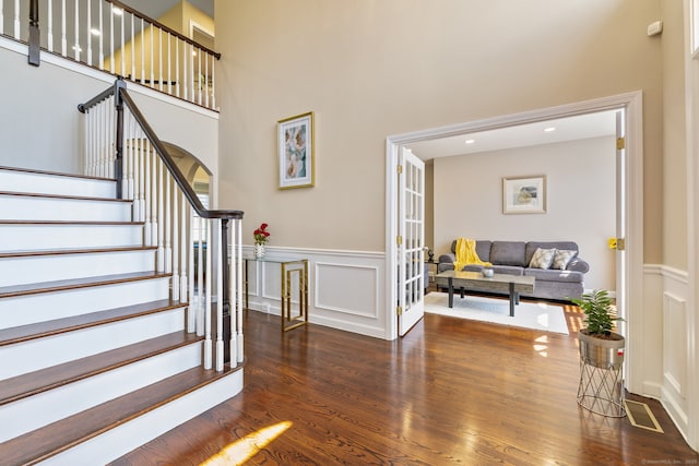 staircase featuring a high ceiling, a wainscoted wall, wood finished floors, and a decorative wall