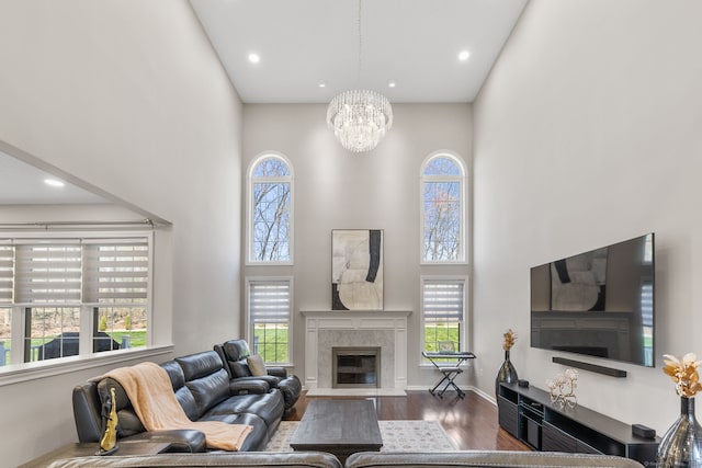 living area featuring wood finished floors, plenty of natural light, a fireplace, a notable chandelier, and a towering ceiling