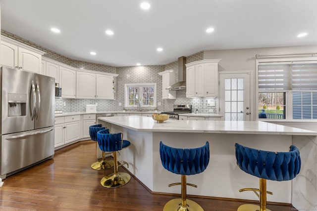 kitchen with a breakfast bar area, a sink, stainless steel appliances, wall chimney exhaust hood, and dark wood-type flooring