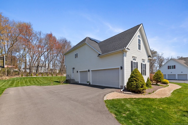 view of side of home with roof with shingles, aphalt driveway, an attached garage, and a lawn