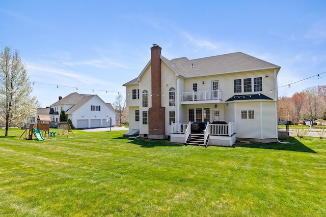 back of property featuring a lawn, a chimney, a balcony, and a playground