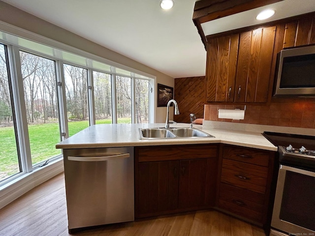 kitchen featuring appliances with stainless steel finishes, a sink, light countertops, light wood-style flooring, and a peninsula