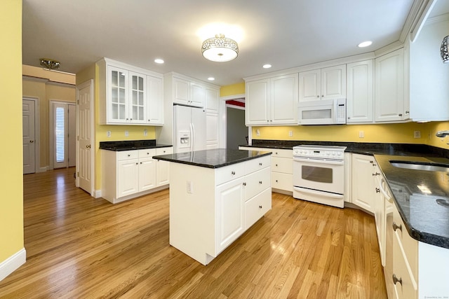 kitchen with white appliances, glass insert cabinets, white cabinets, light wood finished floors, and a sink