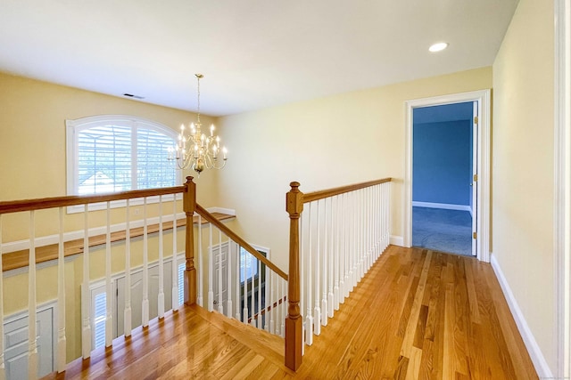 hallway with wood finished floors, an inviting chandelier, an upstairs landing, baseboards, and visible vents