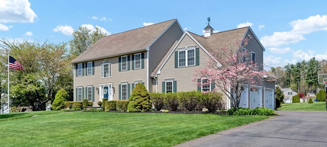 colonial-style house featuring an attached garage, driveway, and a front yard