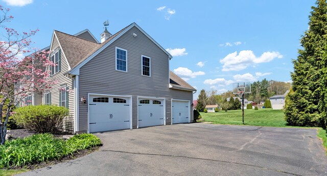 view of side of property featuring a lawn, an attached garage, and aphalt driveway