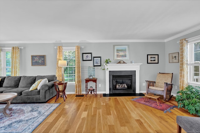 living area with visible vents, a fireplace with flush hearth, baseboards, ornamental molding, and light wood-style flooring