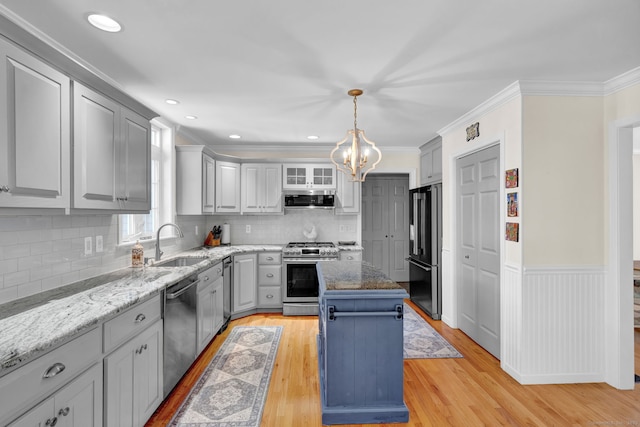 kitchen with appliances with stainless steel finishes, light wood-type flooring, a sink, ventilation hood, and a chandelier