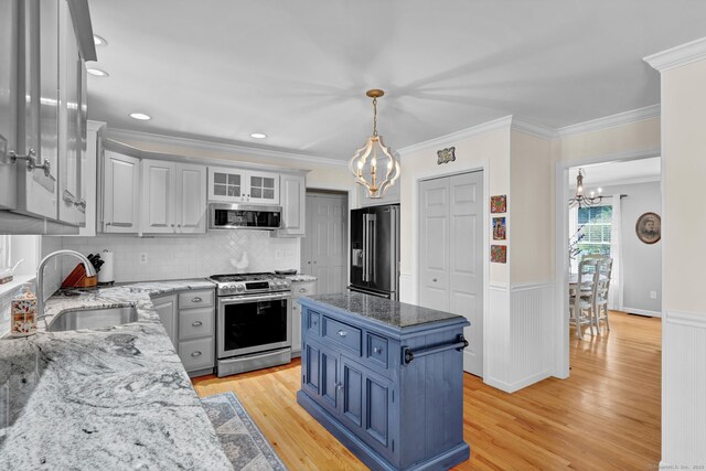 kitchen featuring appliances with stainless steel finishes, a sink, light wood-style floors, blue cabinetry, and a chandelier