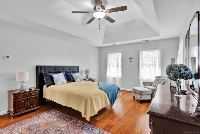 bedroom with visible vents, light wood-style floors, a tray ceiling, and multiple windows
