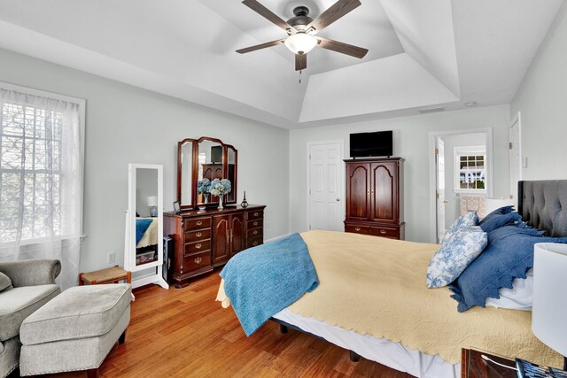 bedroom with a raised ceiling, a ceiling fan, and light wood-style flooring